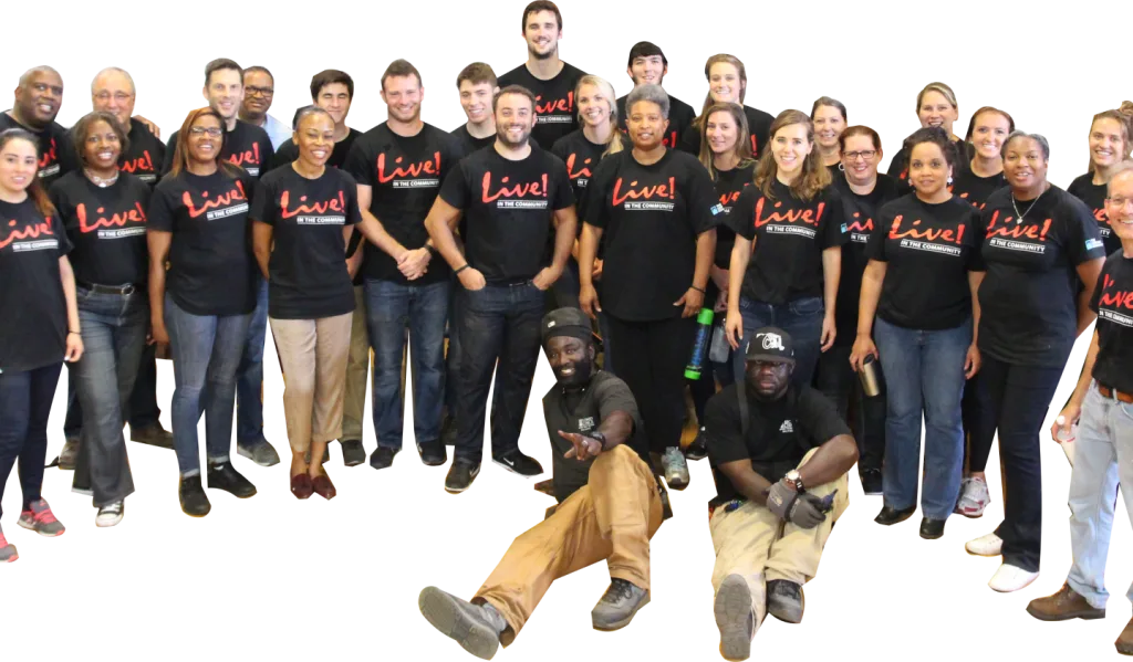 Diverse staff and volunteers from Second Chance, Inc., a Baltimore non-profit, smiling and wearing 'Live! In the Community' t-shirts. This team supports salvaging and reselling used building materials, vintage furniture, antique hardware, and other unique secondhand items for sustainable home improvement projects.