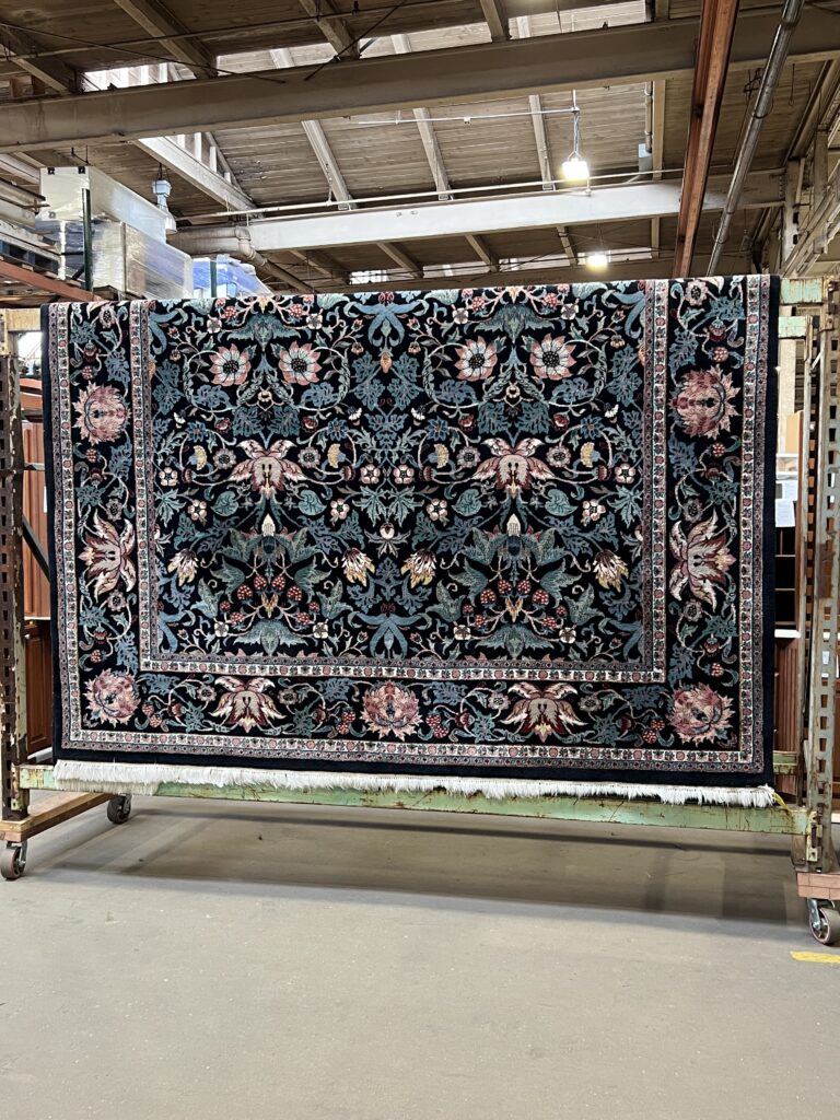 Beautiful vintage floral rug with intricate dark blue, teal, and pink botanical patterns and fringe, a unique secondhand find from Baltimore non-profit, Second Chance, offering sustainable home decor.