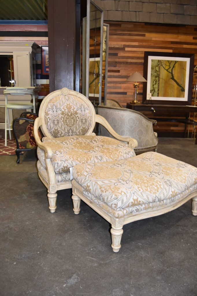 Ornate Marge Carson vintage armchair and matching ottoman with cream and gold patterned upholstery and distressed cream frame. Find unique salvaged secondhand furniture like this at our Baltimore non-profit for sustainable home decor.